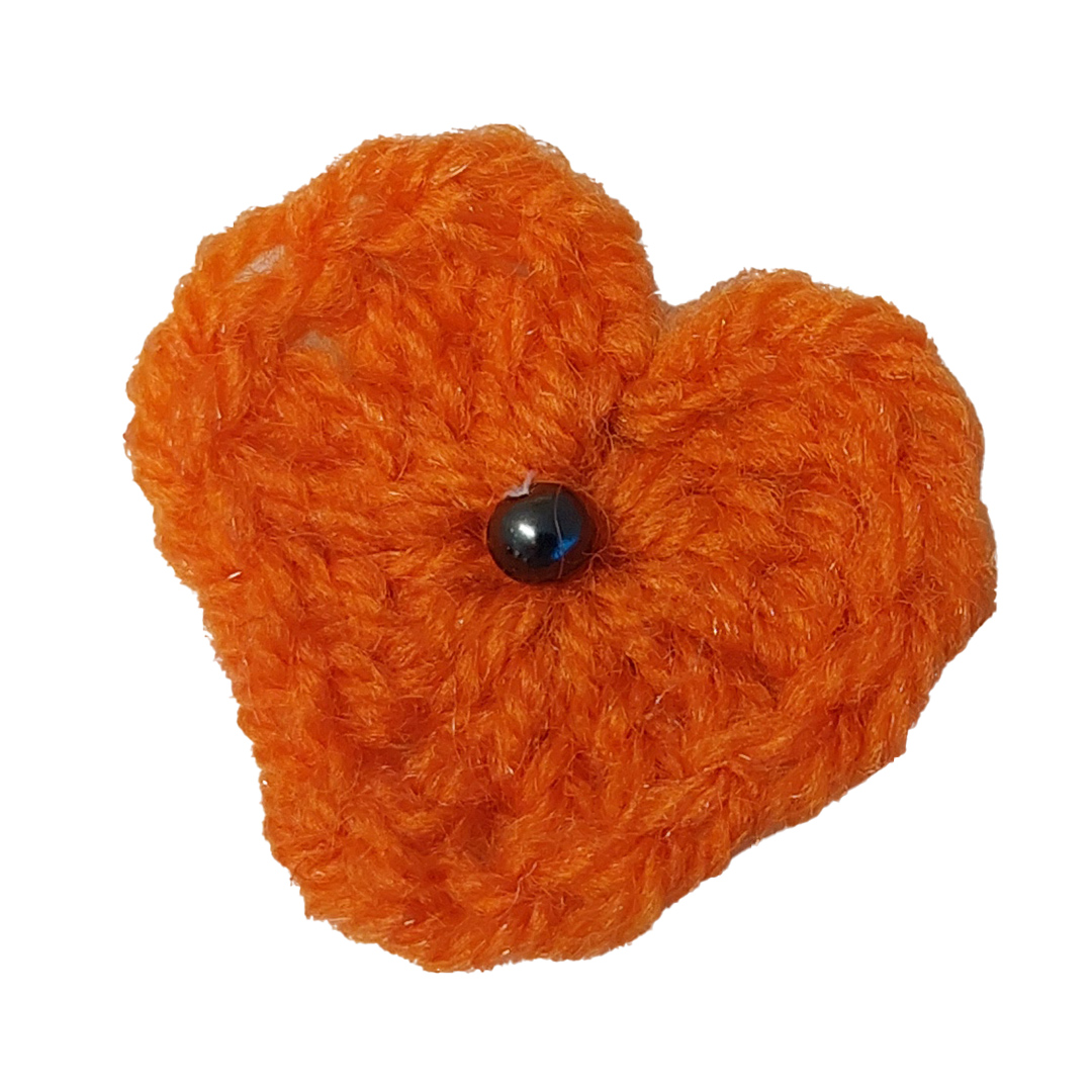 Ett virkat orange hjärta med en svart pärla i mitten.