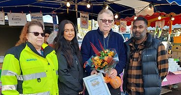 Fyra personer som poserar framför kameran. Pristagaren håller i diplom och blommor.