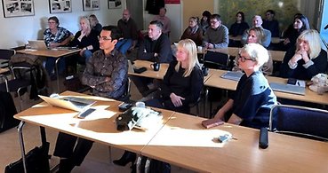 Personer som sitter i ett klassrum och lyssnar på en presentation.